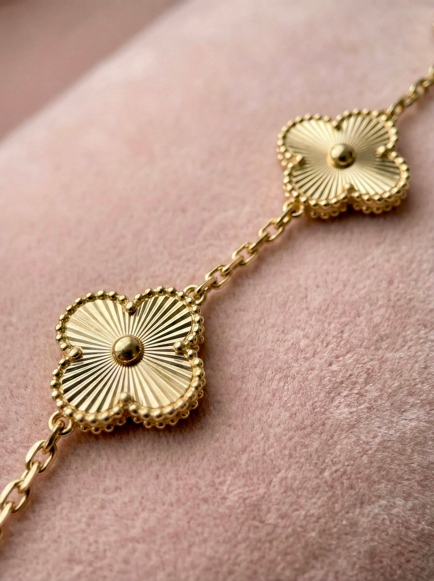Close-up of gold clover charm florielle  bracelet with textured floral detailing