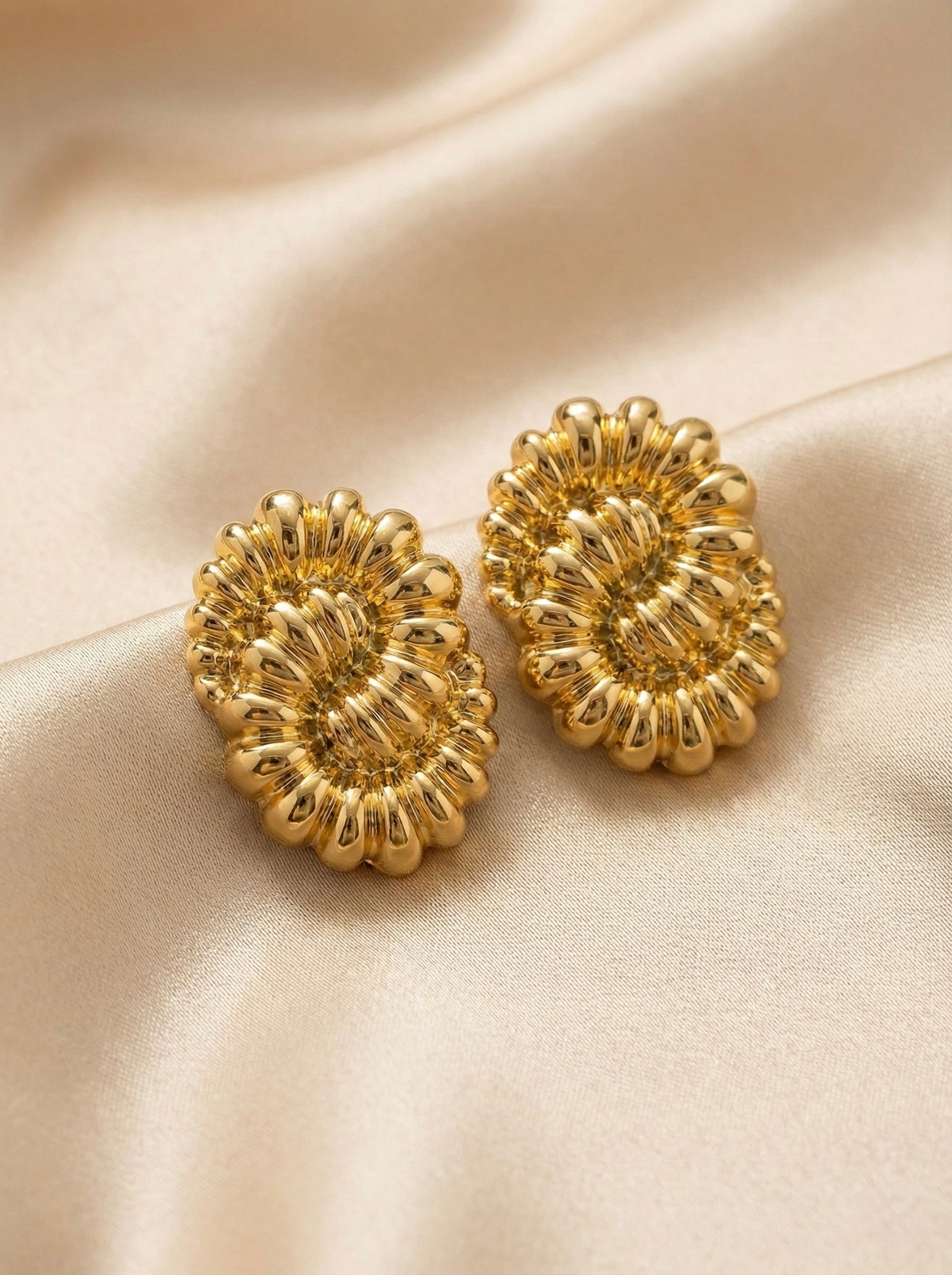 Close-up of bold gold floral stud earrings with sculptural petal texture