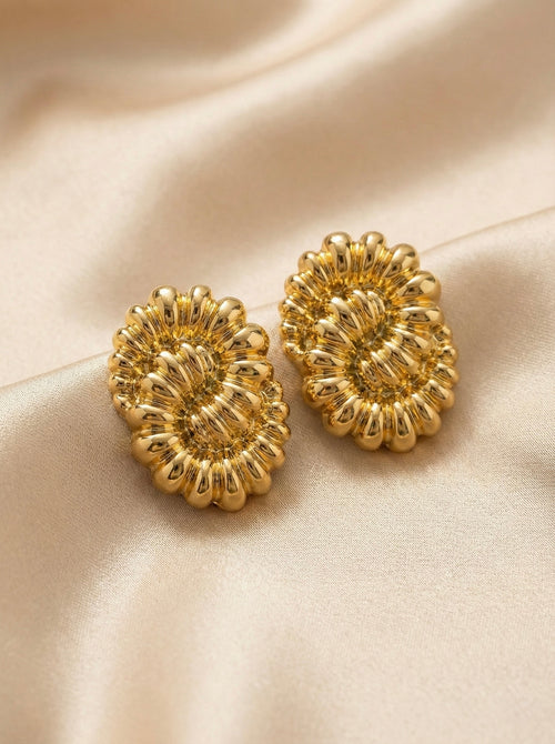 Close-up of bold gold floral stud earrings with sculptural petal texture