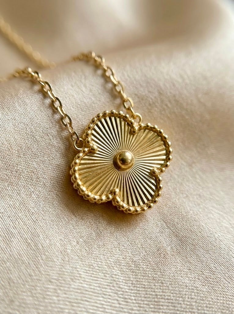 Close-up of gold Florielle clover pendant necklace with textured floral detailing