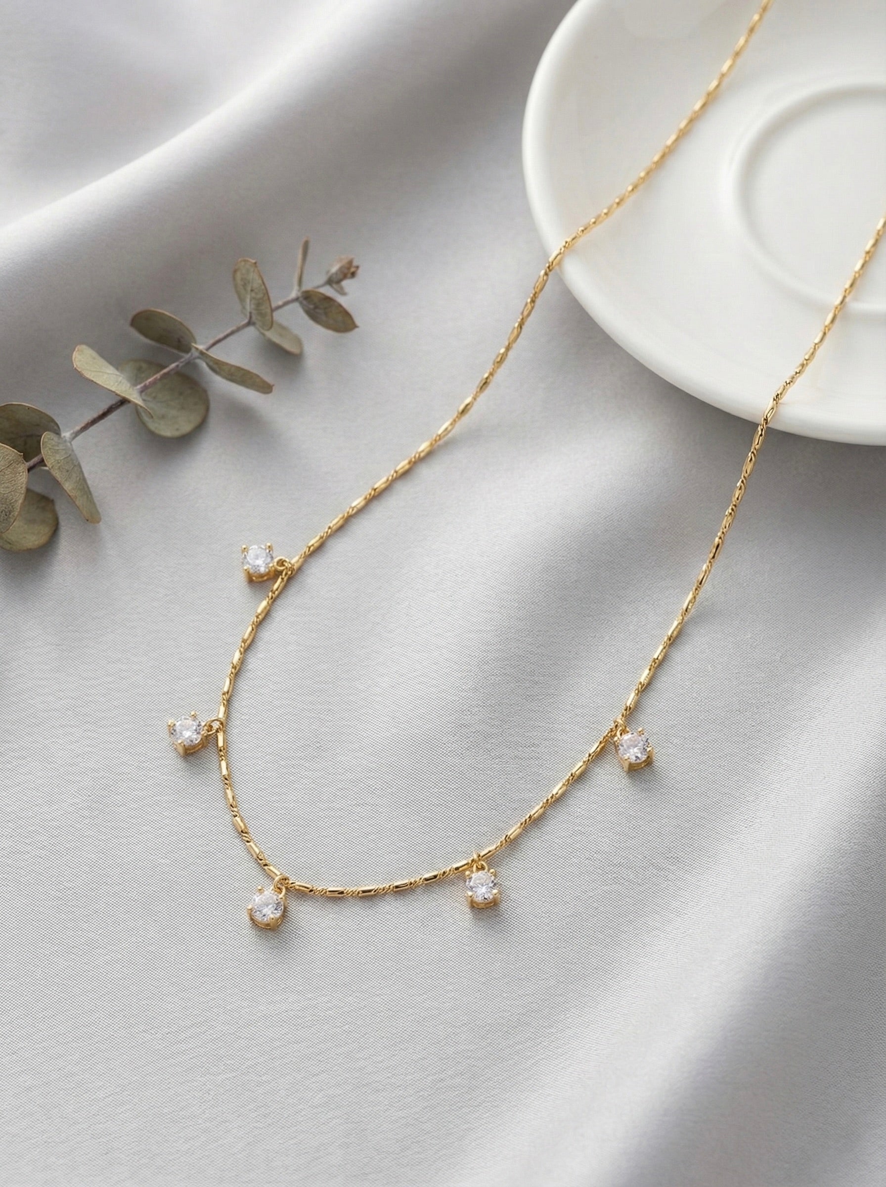 Minimal gold Lyra CZ drop necklace styled on satin fabric for everyday elegance