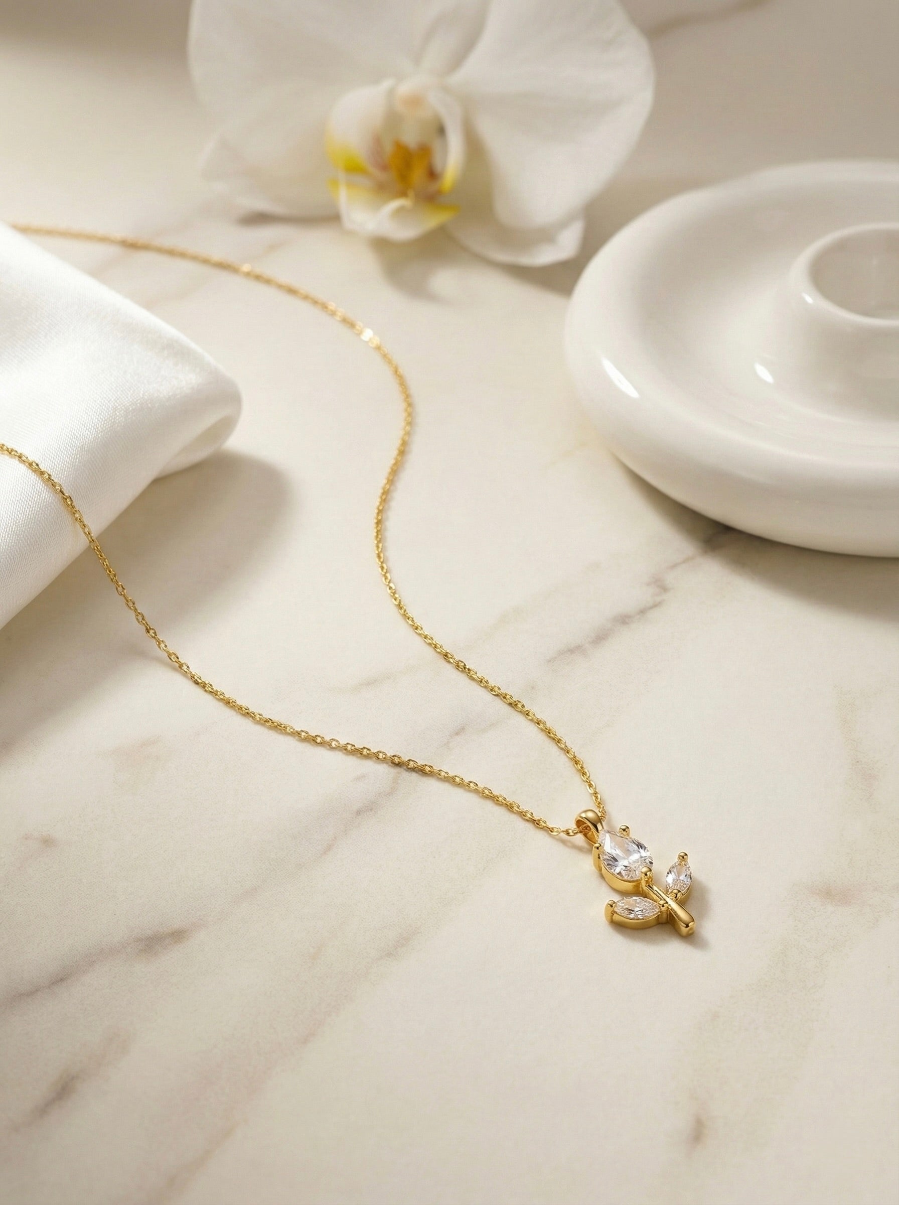 Minimal gold floral floria bud CZ pendant necklace styled on neutral surface for everyday elegance