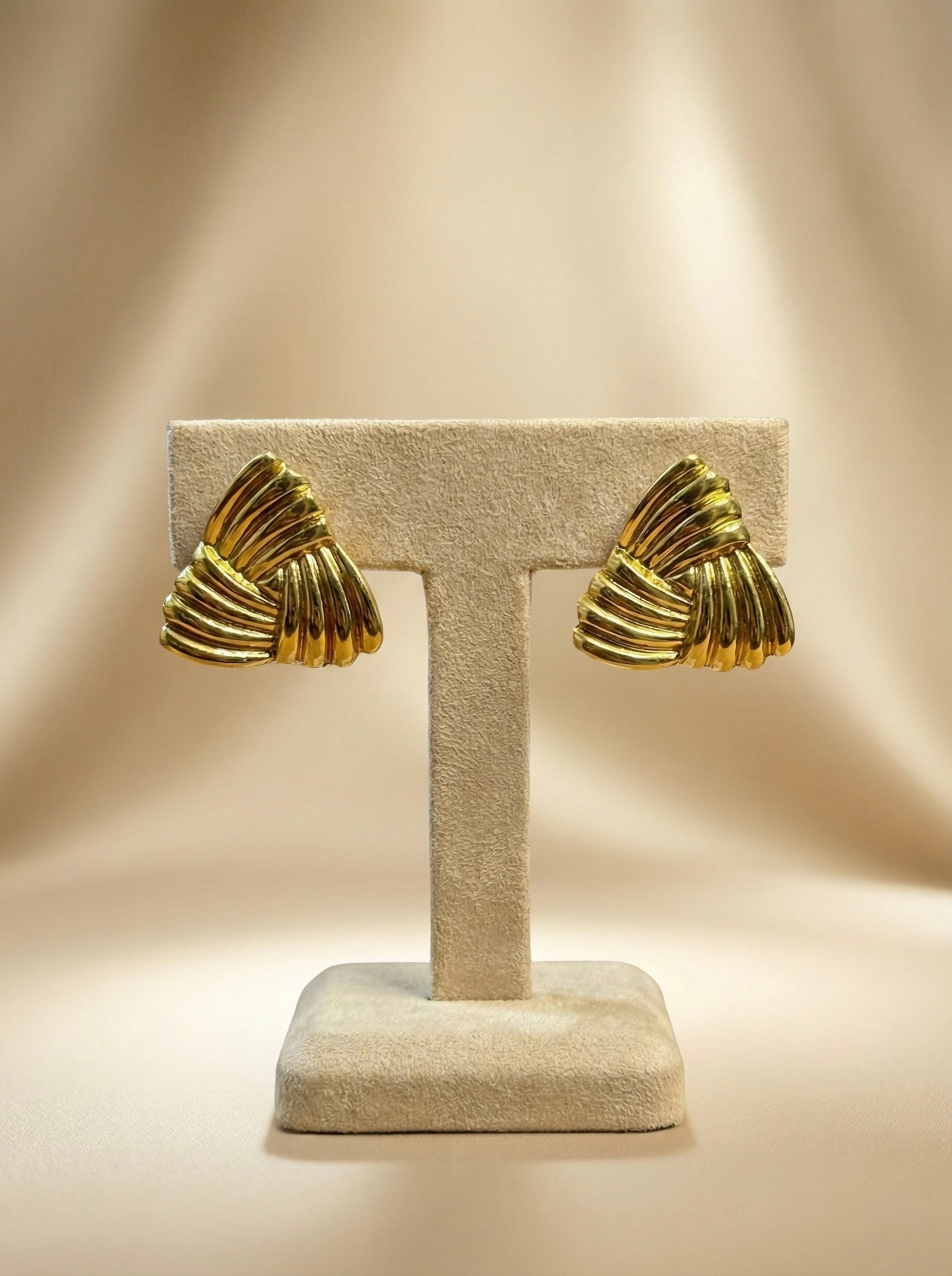 Close-up details on displayed on stand of Velmora sculpted fan gold statement stud earrings showing textured design
